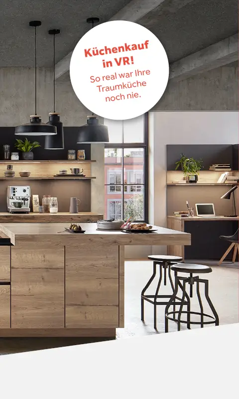 Helle, moderne Küche mit Holzinsel und Barhockern. Im Hintergrund Regale mit Deko und eine Arbeitsfläche mit Laptop am Fenster. Drei schwarze Hängelampen über der Insel. Betonoptik an der Decke.