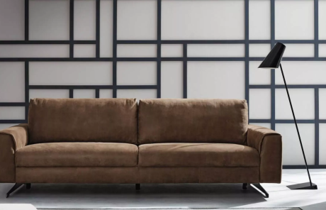 Braunes Sofa vor weißer Wand mit schwarzen geometrischen Linien. Eine schwarze Stehlampe steht rechts vom Sofa.
