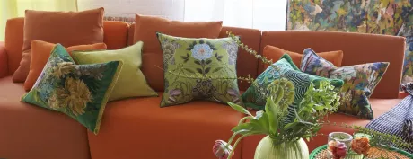 Orangefarbenes Sofa mit grünen und orangefarbenen Zierkissen, dekoriert mit Blumen und Pflanzen.