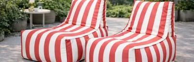 Zwei rot-weiß gestreifte Sitzsäcke stehen auf einer Terrasse. Im Hintergrund grüne Pflanzen und ein kleiner Tisch.
