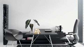 Ein Büro mit einem schwarzen Schreibtisch, einem grauen Stuhl, einer hohen Vase und einer Pflanze. Auf dem Tisch liegen Bücher, ein Laptop, Goldbarren und ein Magazin.