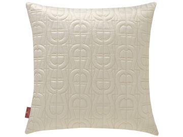 Elfenbeinfarbenes, quadratisches Kissen mit gestepptem, wiederholendem A-förmigen Muster. Eine kleine, rote Marke mit weißem Logo ist an der unteren linken Ecke befestigt.