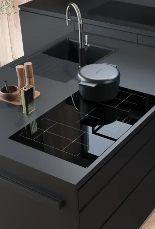 Cuisine moderne gris foncé avec plan de travail, évier et plaque à induction. À gauche de l'évier se trouvent des moulins à épices en bois, un mortier et de l'huile d'olive. Une cocotte en fonte grise sur la plaque de cuisson. Mur en bois.