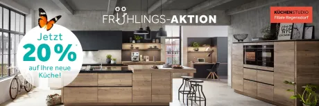 Moderne Küche in Holzoptik mit schwarzen Akzenten, Insel, Tresen und zwei Öfen. Im Vordergrund eine orangefarbene Schmetterling und ein Fahrrad. Frühlings-Aktion.