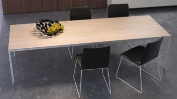 Ein Esstisch mit vier Stühlen steht auf einem grauen Boden. Auf dem Tisch steht eine Schale mit Trauben. Die Tischplatte ist hell, die Stühle sind schwarz mit weissen Metallbeinen.