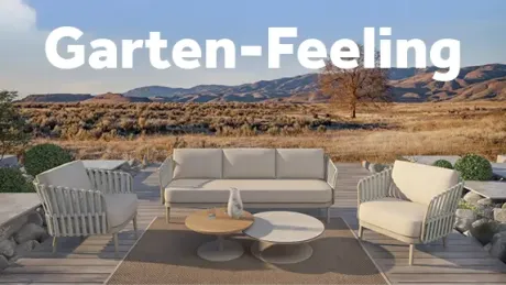 Moderne Outdoor-Loungegruppe auf Holzterrasse vor sonniger Berglandschaft. Beiges Dreisitzer-Sofa und zwei Sessel auf Teppich, dazu zwei runde Couchtische mit Deko. Im Hintergrund trockene Büsche, Bäume, Hügel und blauer Himmel.