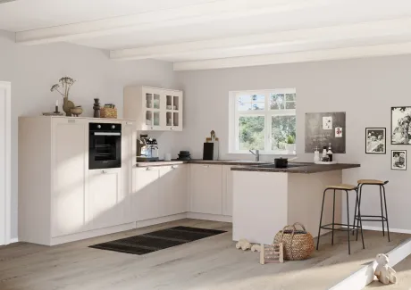 Cuisine moderne en L dans des tons beiges clairs, avec des plans de travail foncés et des poutres apparentes. Fenêtre donnant sur la verdure. Équipée d'un four encastré, d'une cafetière, d'un îlot avec évier et plaque de cuisson. Photos et jouets.
