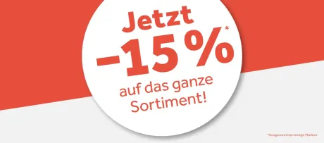 Werbeplakat mit rotem Text "Jetzt -15% auf das ganze Sortiment!" auf weißem Kreis, der sich von einem roten und weißen Hintergrund abhebt. Unten rechts steht klein "Ausgenommen einige Marken".