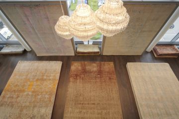 Innenaufnahme mit Teppichen auf dem Boden und an der Wand, beleuchtet von einem großen Kronleuchter. Draußen ein Fenster mit Blick auf einen Parkplatz.