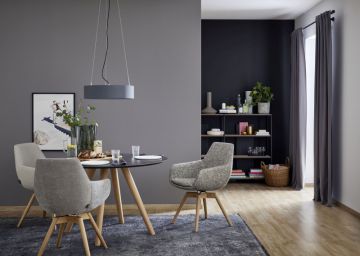 Ein Esszimmer mit runden Tisch, drei Stühlen, einer Hängelampe, einem Regal und einem Fenster mit Vorhang. Die Wände sind in Grau- und Blautönen gehalten und der Boden ist helles Holz.