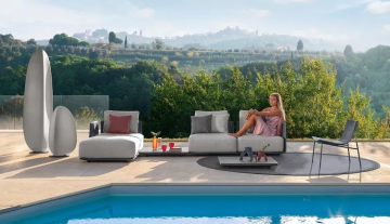 Draufsicht auf Terrasse mit Pool, Frau auf Sofa vor Hügellandschaft. Moderne Möbel, darunter skulpturale Objekte. Heitere Atmosphäre.