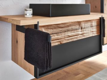 Nahaufnahme eines Badezimmerschranks mit einem schwarzen Waschbecken, einem schwarzen Handtuch und einer Duftkerze. Der Schrank hat eine Holzfront mit markanter Maserung und einen schwarzen unteren Teil.