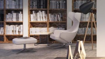 Ein Interieur mit einem weißen Sessel, einem Hocker mit Buch, einem kleinen Tisch und einer Stehlampe vor einem Bücherregal. Im Vordergrund stehen Vasen.