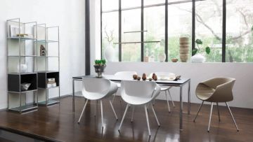 Esszimmer mit Tisch, Stühlen, Regal und großem Fenster. Der Tisch ist mit Geschirr und Dekoration gedeckt. Das Regal hat offene Fächer und Glasböden. Der Boden ist aus dunklem Holz.