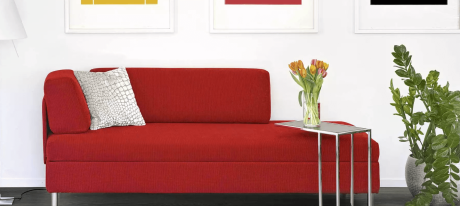 Rotes Sofa mit gemustertem Kissen, Tisch mit Tulpen und Topfpflanze vor weißer Wand mit Bildern.