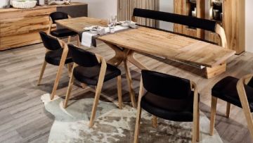 Ein heller Essbereich mit Holztisch, Stühlen mit schwarzen Sitzen und Rückenlehnen, einer Sitzbank und einem Teppich. Der Tisch ist mit Geschirr dekoriert.