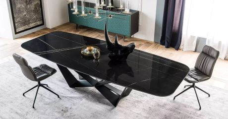 Eleganter Essbereich mit schwarzem Marmortisch, dessen extravagantes Untergestell ins Auge fällt. Darauf eine Rhinozeros-Skulptur. Zwei Ledersessel flankieren den Tisch auf einem hellen Teppich.