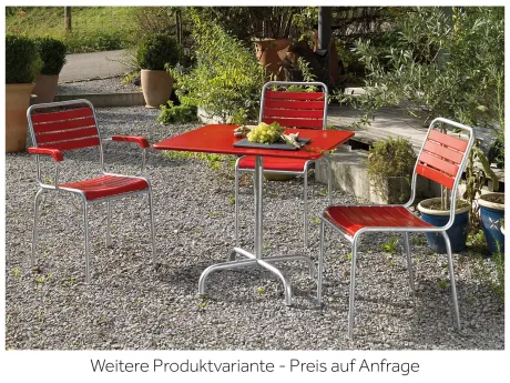 Roter Gartentisch mit drei passenden Stühlen auf Kies. Auf dem Tisch liegen Weintrauben und Brot. Im Hintergrund grüne Pflanzen.